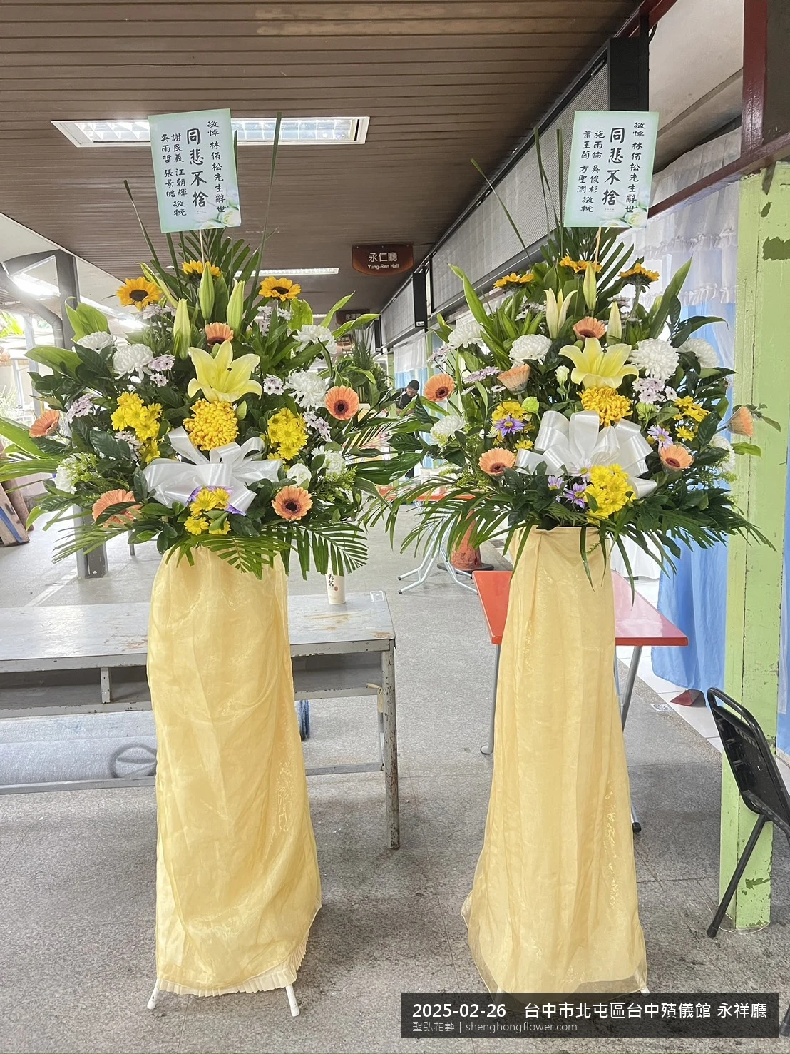 冬末濕冷氣候下高架白菊花籃並陳，雙層花籃結構、上層紅玫瑰下層白菊，送達台中北屯台中殯儀館 永祥廳前後整體寧靜哀思，傳達家屬最後敬意，聖弘花藝在地團隊現場實拍照。