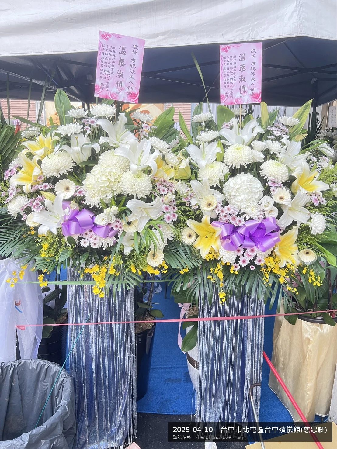 台中北屯台中殯儀館(慈忠廳)前氣氛安寧整齊，選用白菊喪禮花籃並黃白雙色配置、字牌面向訪客，搭配春末穀雨時節氣候溫暖偏濕的場景，撫慰家屬不捨之情，聖弘花藝在地團隊現場實拍照。