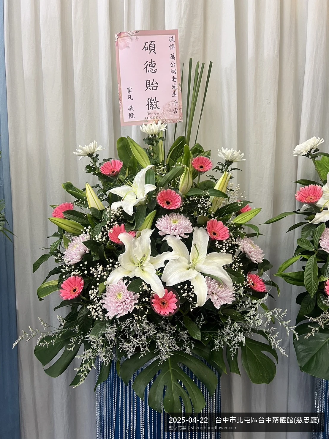 台中北屯台中殯儀館(慈忠廳)前氣氛素雅莊重，選用白菊喪禮花籃並黃白雙色配置、字牌面向訪客，搭配春末穀雨時節氣候溫暖偏濕的場景，撫慰家屬不捨之情，聖弘花藝在地團隊現場實拍照。