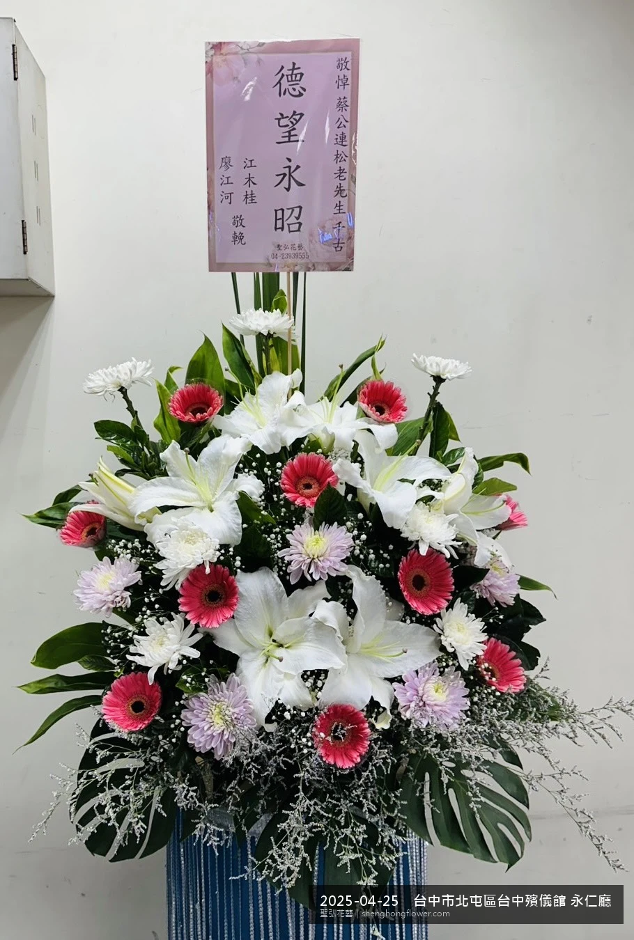 台中北屯台中殯儀館 永仁廳前置高架白菊花籃，氛圍沉靜典雅。挑高花架穩固、字牌方向清晰，於春末穀雨時節氣候溫暖偏濕就位完成，陪伴家屬度過難捨時刻，聖弘花藝在地團隊現場實拍照。