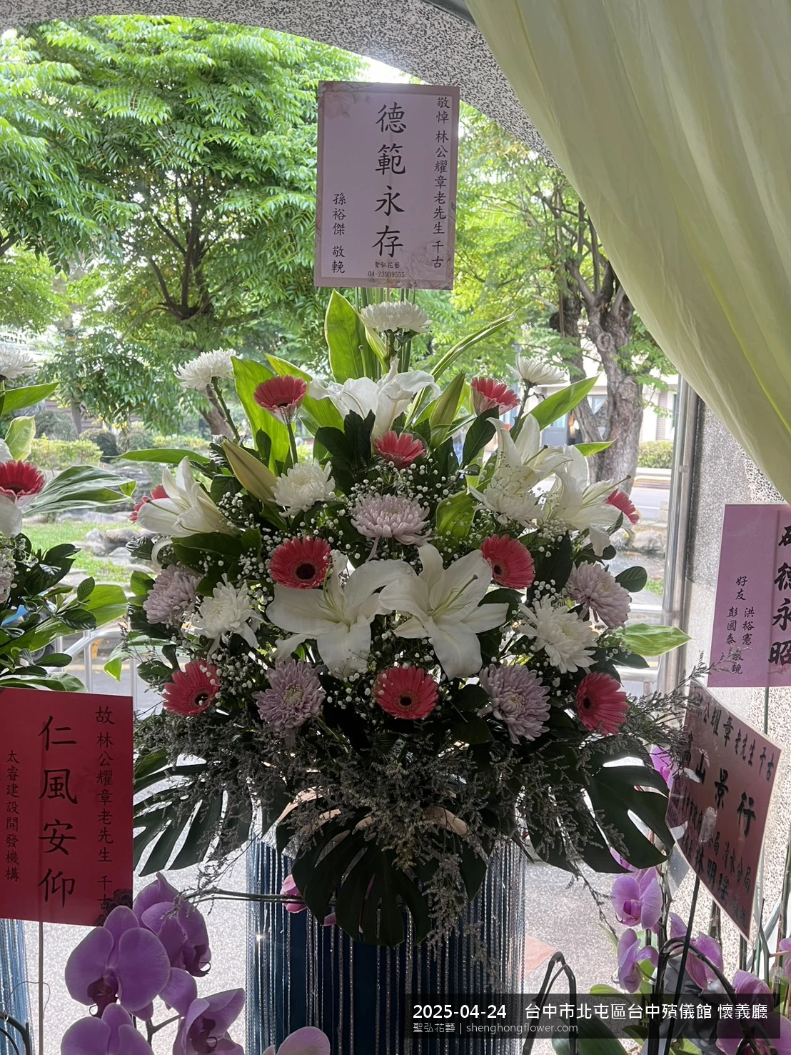 春末穀雨時節氣候溫暖偏濕下，台中北屯台中殯儀館 懷義廳前光線柔和。我們選用高架白菊花籃，雙劍蘭挑高、黃菊鋪底，現場顯得安寧整齊，誠摯傳達對家屬的關懷，聖弘花藝在地團隊現場實拍照。