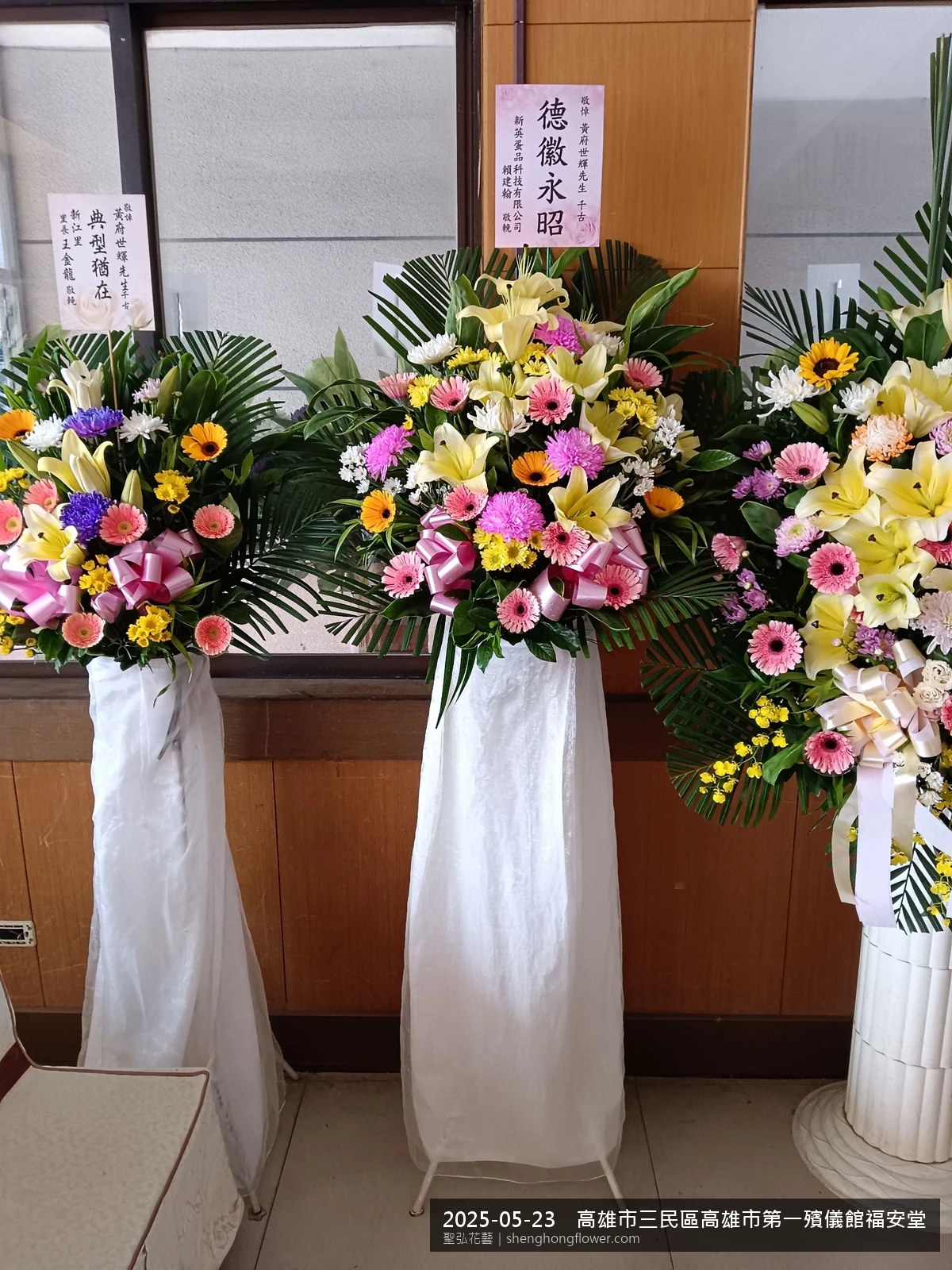 高雄三民高雄市第一殯儀館福安堂前置高架白菊花籃，氛圍現場端正。挑高花架穩固、字牌方向清晰，於初夏暖陽氣候宜人就位完成，依指定方位整齊就位，聖弘花藝在地團隊現場實拍照。