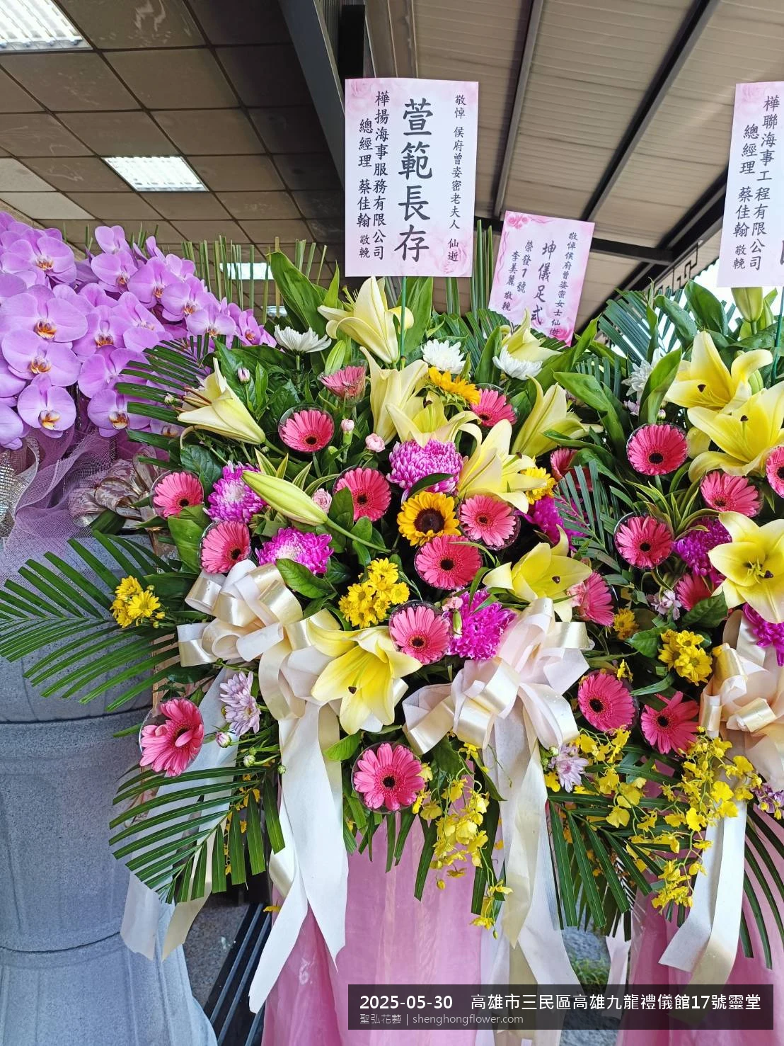高雄三民高雄九龍禮儀館靈堂現場置高架白菊花籃，氛圍配置妥當。挑高花架穩固、字牌方向清晰，於初夏暖陽氣候宜人就位完成，於現場完成定位，聖弘花藝在地團隊現場實拍照。