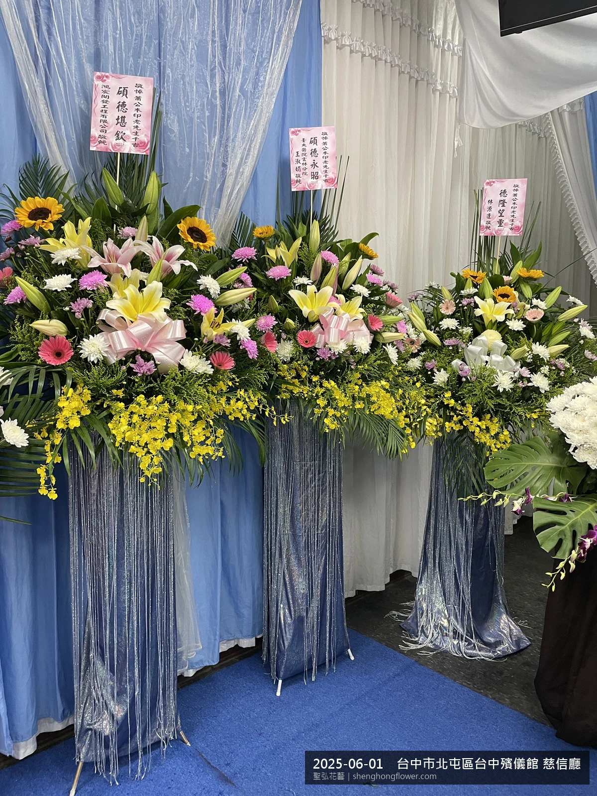 盛夏午後氣候炎熱下，台中北屯台中殯儀館 慈信廳前光線柔和。我們選用高架白菊花籃，雙劍蘭挑高、黃菊鋪底，現場顯得寧靜哀思，誠摯傳達對家屬的關懷，聖弘花藝在地團隊現場實拍照。