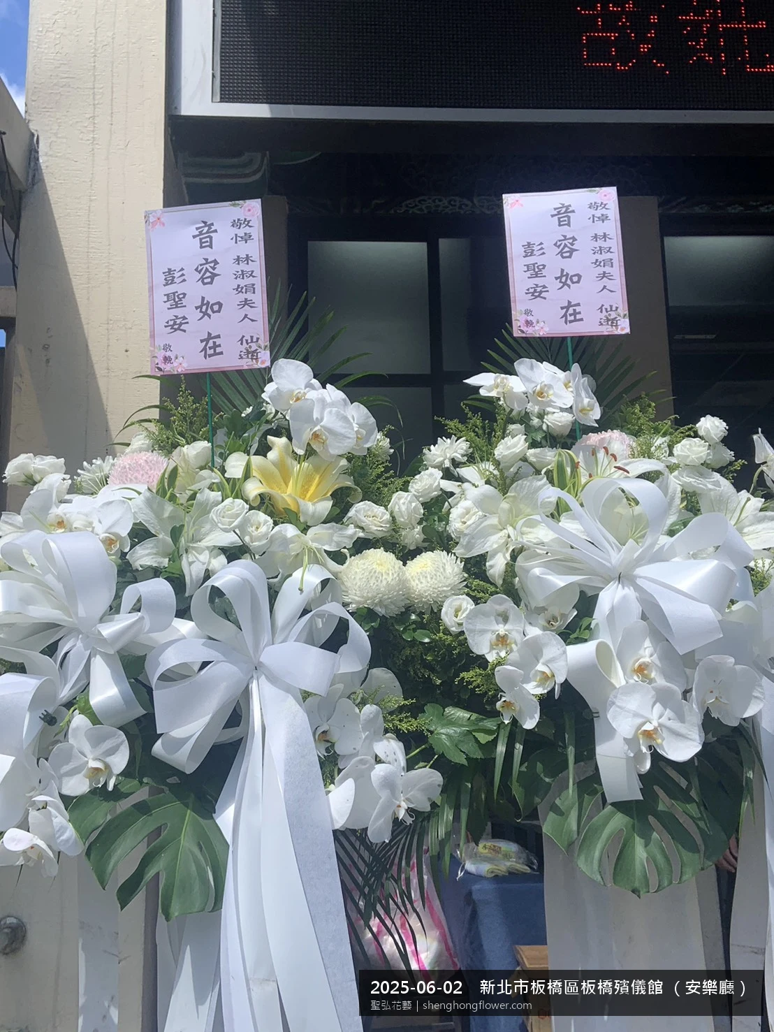 盛夏午後氣候炎熱下高架白菊花籃並陳，雙層花籃結構、上層紅玫瑰下層白菊，送達新北板橋板橋殯儀館 （安樂廳）前後整體現場端正，依指定方位整齊就位，聖弘花藝在地團隊現場實拍照。