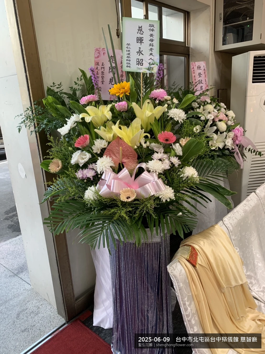 盛夏午後氣候炎熱下，台中北屯台中殯儀館 慈智廳前光線柔和。我們選用高架白菊花籃，雙劍蘭挑高、黃菊鋪底，現場顯得沉靜典雅，誠摯傳達對家屬的關懷，聖弘花藝在地團隊現場實拍照。