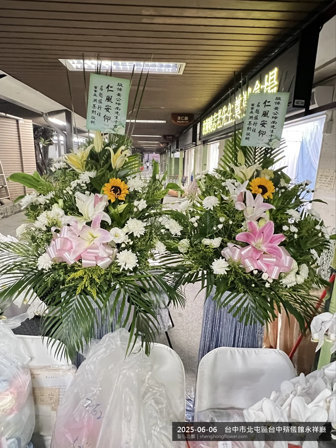 盛夏午後氣候炎熱下高架白菊花籃並陳，雙層花籃結構、上層紅玫瑰下層白菊，送達台中北屯台中殯儀館永祥廳前後整體寧靜哀思，傳達家屬最後敬意，聖弘花藝在地團隊現場實拍照。