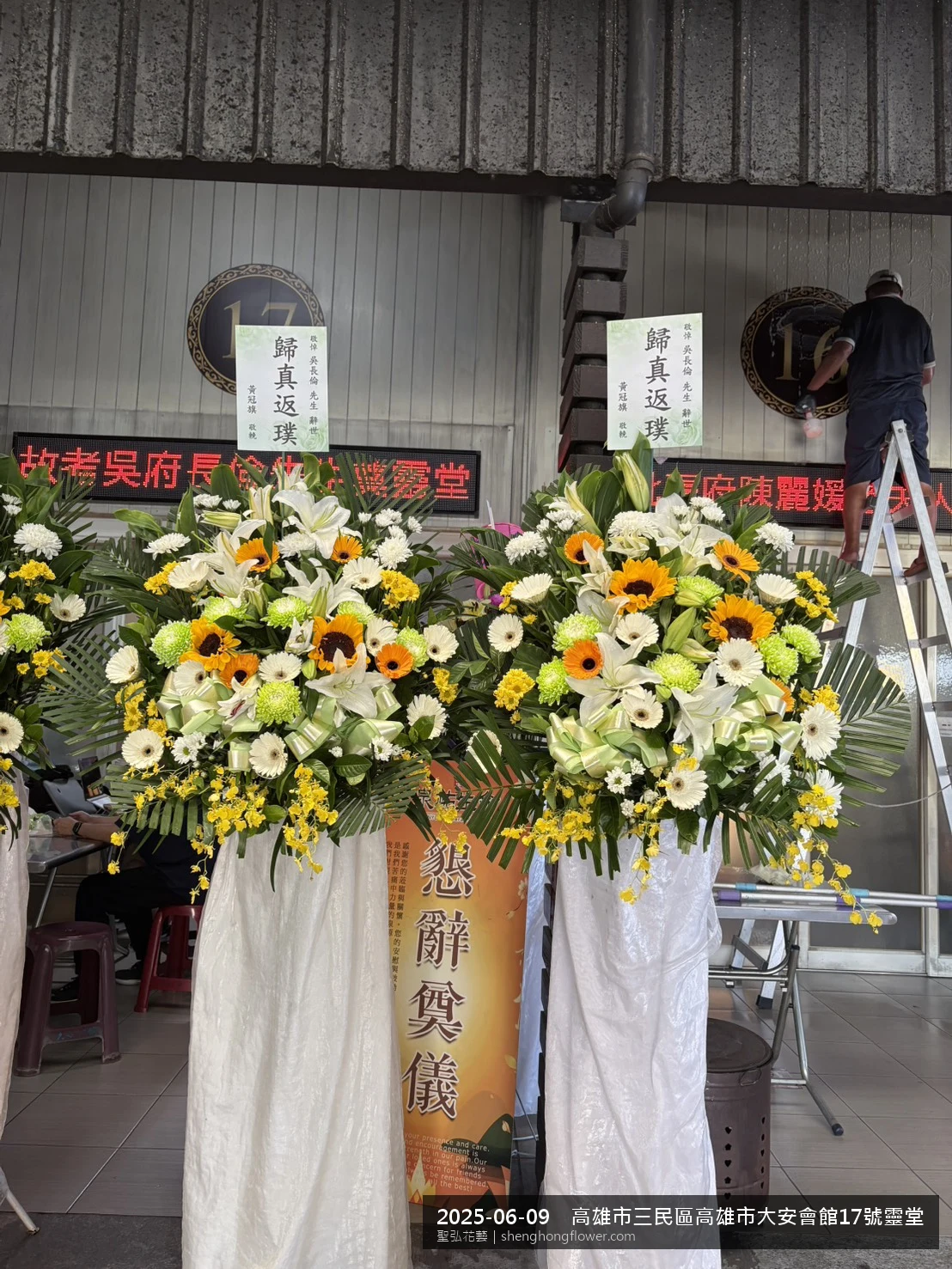 高雄三民高雄市大安會館靈堂現場置高架白菊花籃，氛圍陳設整齊。挑高花架穩固、字牌方向清晰，於盛夏午後氣候炎熱就位完成，依指定方位整齊就位，聖弘花藝在地團隊現場實拍照。
