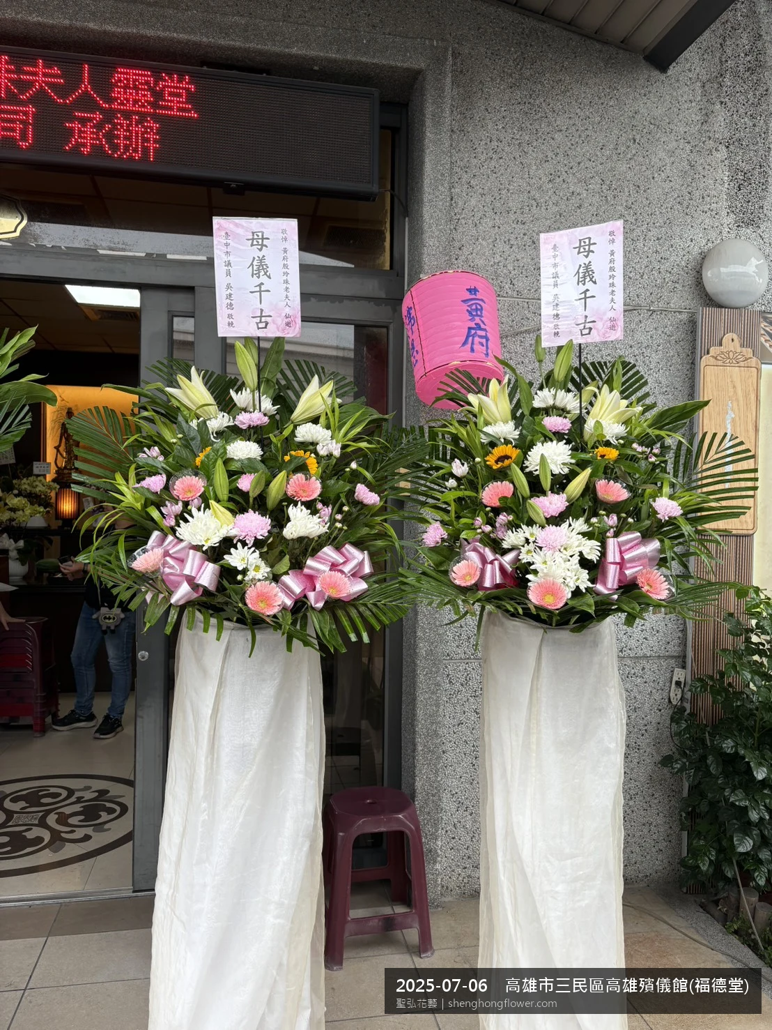 盛夏陽光氣候悶熱下高架白菊花籃並陳，雙層花籃結構、上層紅玫瑰下層白菊，送達高雄三民高雄殯儀館(福德堂)前後整體整潔有序，於現場完成定位，聖弘花藝在地團隊現場實拍照。
