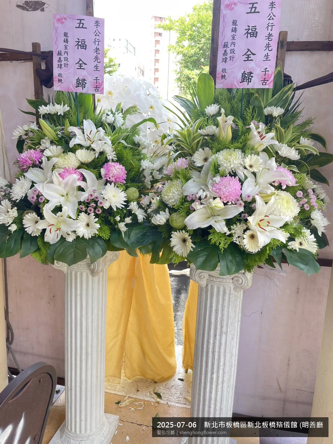 新北板橋新北板橋殯儀館 (明善廳)前置高架白菊花籃，氛圍配置妥當。挑高花架穩固、字牌方向清晰，於盛夏陽光氣候悶熱就位完成，依指定方位整齊就位，聖弘花藝在地團隊現場實拍照。