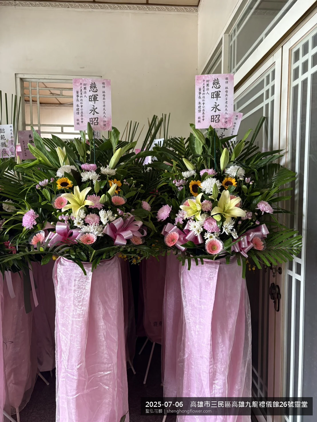 高雄三民高雄九龍禮儀館靈堂現場置高架白菊花籃，氛圍配置妥當。挑高花架穩固、字牌方向清晰，於盛夏陽光氣候悶熱就位完成，配合主人家完成擺設，聖弘花藝在地團隊現場實拍照。