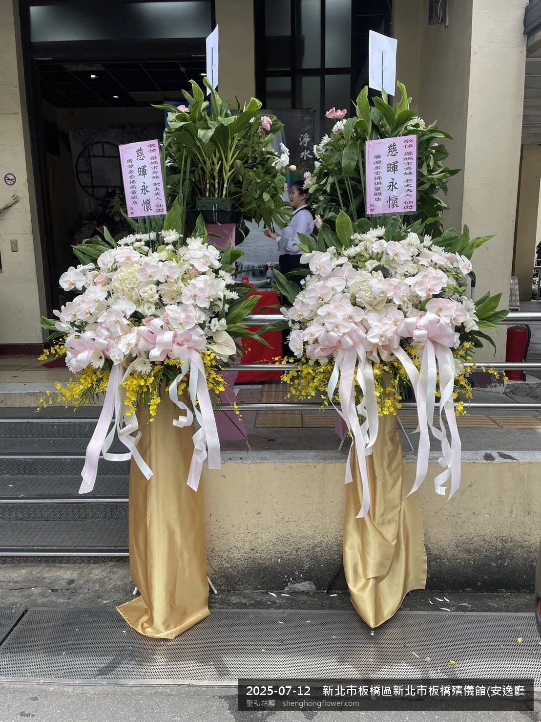 盛夏陽光氣候悶熱下高架白菊花籃並陳，雙層花籃結構、上層紅玫瑰下層白菊，送達新北板橋新北市板橋殯儀館(安逸廳)前後整體整潔有序，配合主人家完成擺設，聖弘花藝在地團隊現場實拍照。