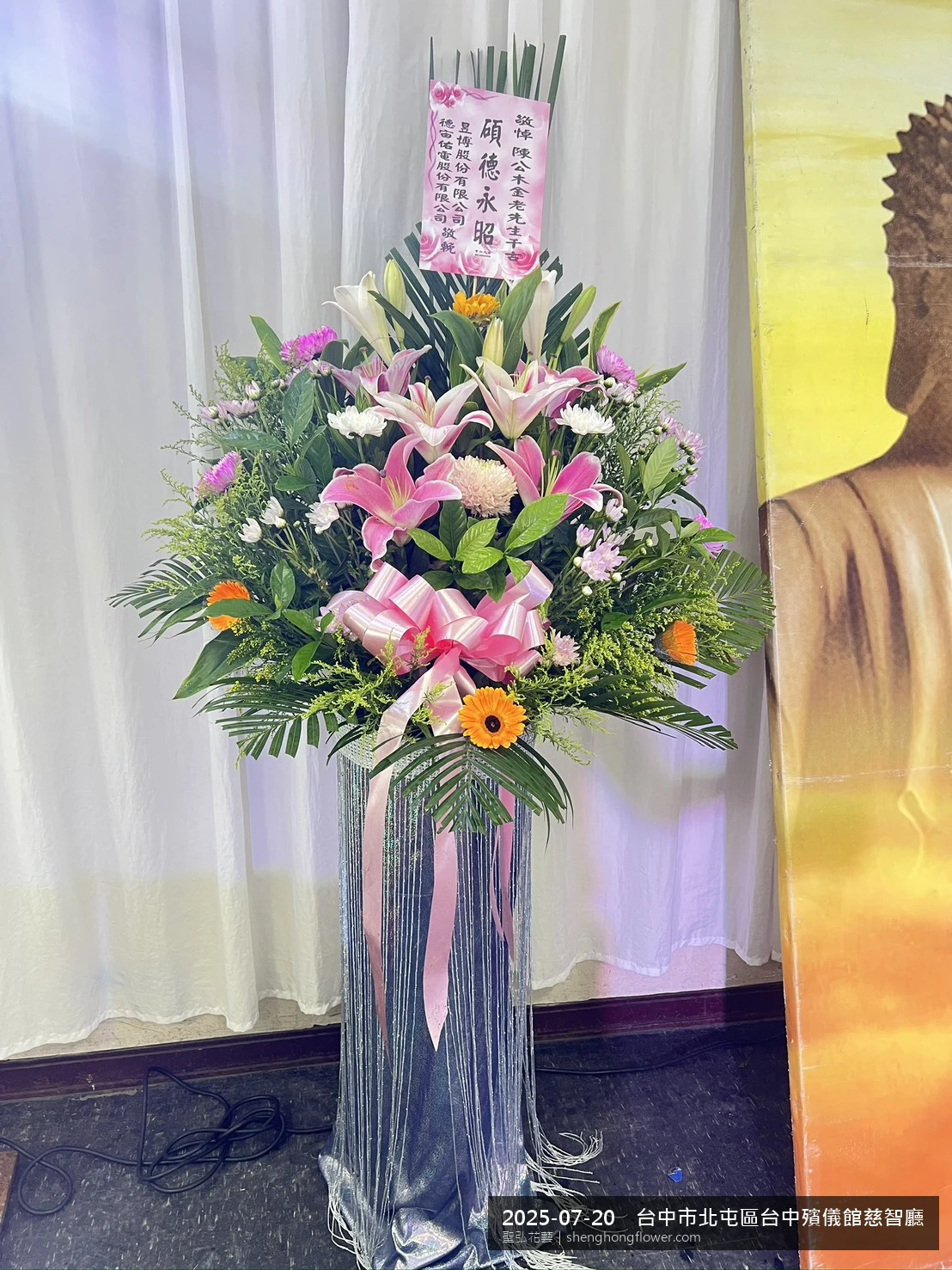 高架白菊花籃主花百合配劍蘭、底部黃菊填充，於盛夏陽光氣候悶熱花朵保鮮極佳。送達台中北屯台中殯儀館慈智廳前後完成擺設，安寧整齊，寄託家屬哀思敬意，聖弘花藝在地團隊現場實拍照。