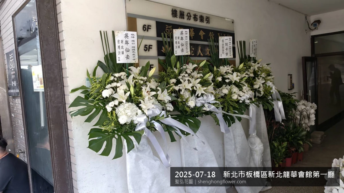 高架白菊花籃主花百合配劍蘭、底部黃菊填充，於盛夏陽光氣候悶熱花朵保鮮極佳。送達新北板橋新北龍華會館第一廳現場後完成擺設，陳設整齊，於現場完成定位，聖弘花藝在地團隊現場實拍照。