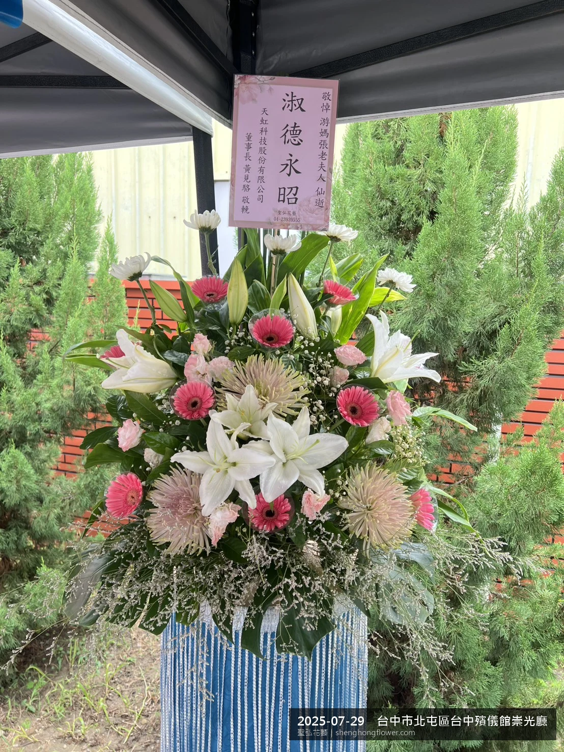 台中北屯台中殯儀館崇光廳前氣氛沉靜典雅，選用高架白菊花籃並高架支架對稱、白菊圍裙裝飾，搭配盛夏陽光氣候悶熱的場景，撫慰家屬不捨之情，聖弘花藝在地團隊現場實拍照。