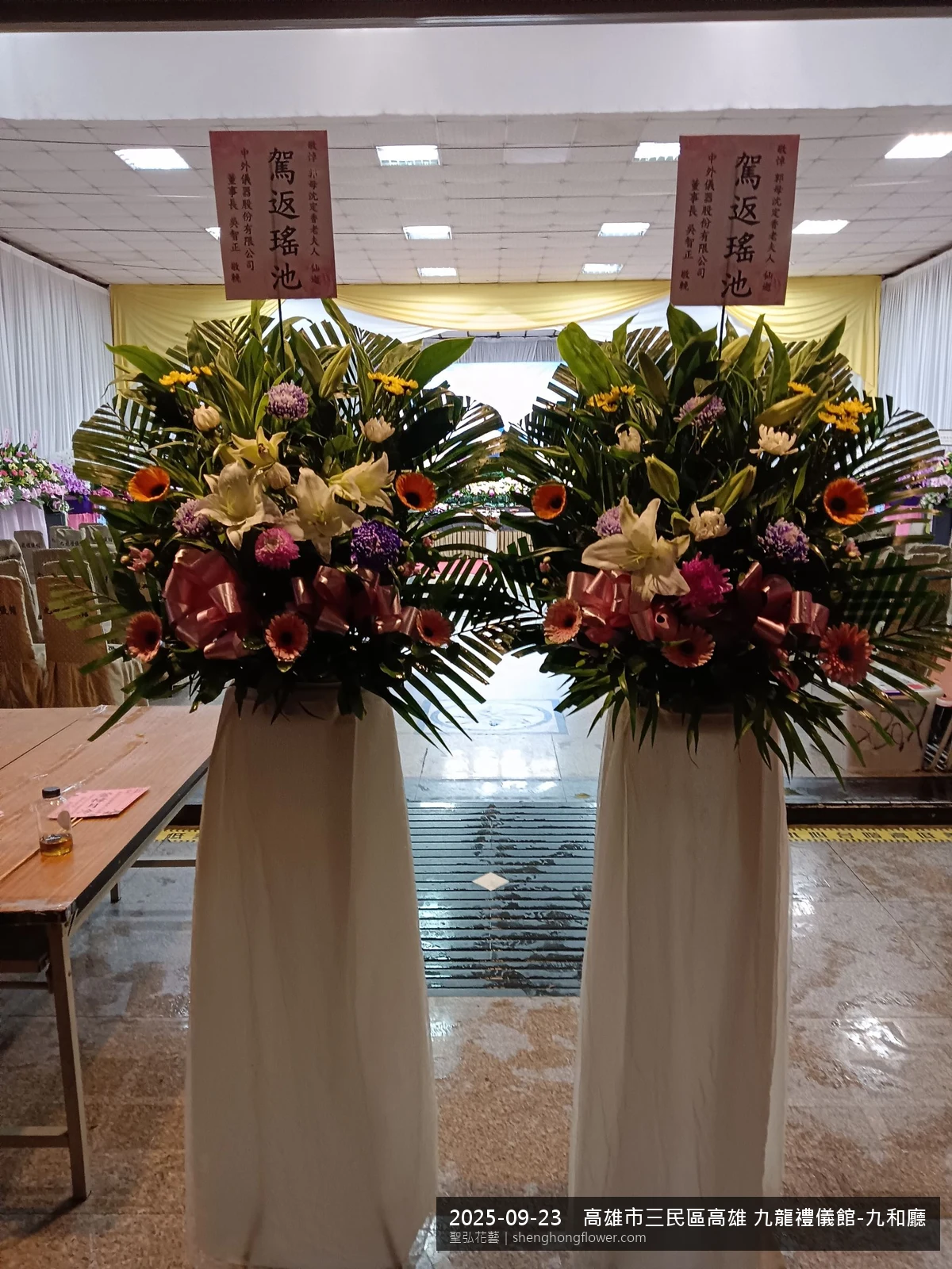 初秋微涼氣候轉爽下高架白菊花籃並陳，雙層花籃結構、上層紅玫瑰下層白菊，送達高雄三民高雄 九龍禮儀館-九和廳現場後整體陳設整齊，於現場完成定位，聖弘花藝在地團隊現場實拍照。