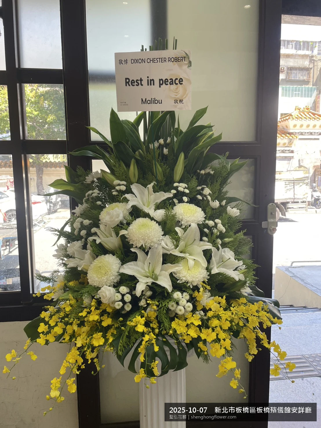 高架白菊花籃主花百合配劍蘭、底部黃菊填充，於深秋舒爽氣候涼風花朵保鮮極佳。送達新北板橋板橋殯儀館安詳廳前後完成擺設，現場端正，依指定方位整齊就位，聖弘花藝在地團隊現場實拍照。